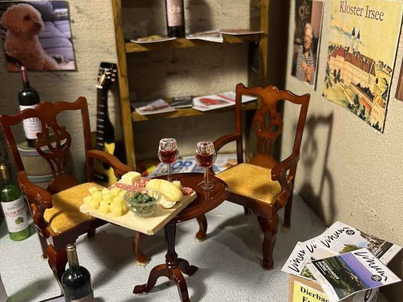 Detailaufnahme eines Tisches im Diorama, mit Weingläsern, die mit Rotwein halb gefüllt sind und vielem mehr, wie Käse, Brot...