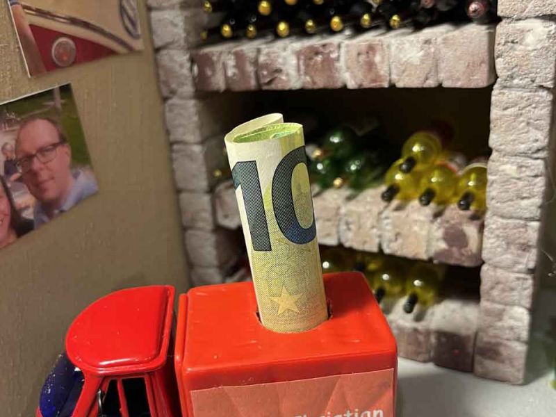 Eine Piaggio Ape in Rot mit Rotem Kastenaufbau. Aus diesem ragen nach oben 100 € Geldscheine heraus.